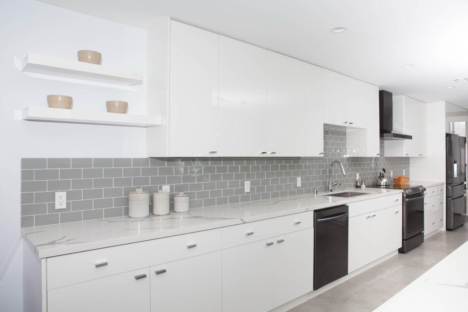 White kitchen remodel by IAS Boutique Remodeling with a marble-look quartz waterfall island and gray glass subway backsplash.