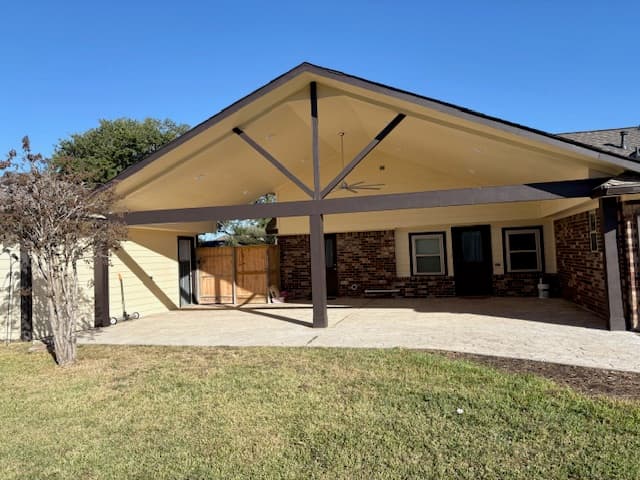 Painted gable patio cover with a ceiling fan over a concrete patio on a brick home.