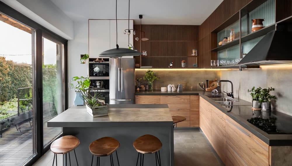 Modern kitchen with wood-slat walls, a concrete-look island with bar stools, and sliding doors to a garden.