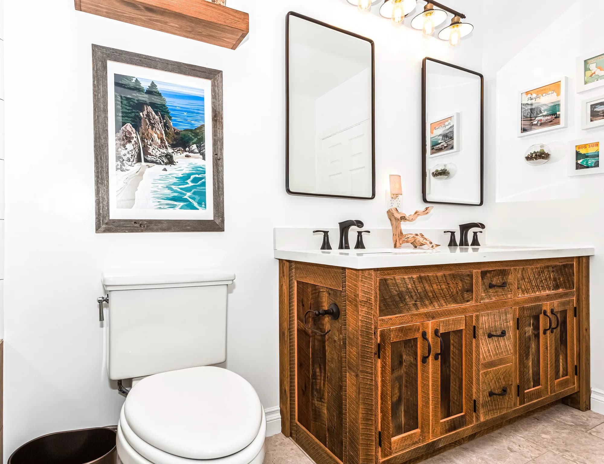 Bathroom with a rustic reclaimed-wood double vanity, white quartz counters, black-framed mirrors, matte-black faucets, and framed coastal artwork.