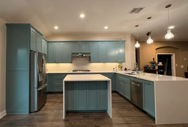 Teal-cabinet kitchen with a white quartz island, a gas cooktop, stainless refrigerator and dishwasher, and dark wood-look flooring.