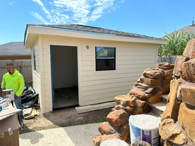 Detached room addition under construction in a Houston backyard, with new fiber-cement siding and a shingle roof.